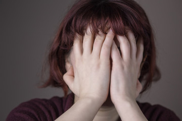 Red-haired woman having a headache or being embarrassed. Hands over the face. Human facial expression, emotion, feeling, sign symbol body language