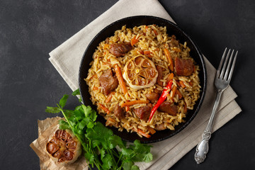 Oriental cuisine. Uzbek pilaf or plov from rice and meat in a cast iron pan on wooden rustic board. Top view.