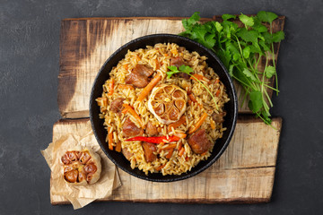 Oriental cuisine. Uzbek pilaf or plov from rice and meat in a cast iron pan on wooden rustic board. Top view.