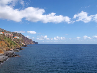 bright sunlit view of the coast at funchal madeira with a bright blue calm sunlit sea and summer sky with white clouds