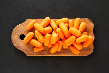 Fresh baby carrots on rustic wooden board on black surface, top view. Overhead, from above, flat lay.