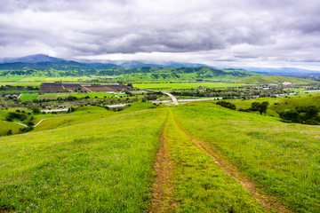 Fototapeta na wymiar Hiking trail descending into the valley; Aerial view of agricultural fields and mountains in the background, south San Francisco bay, San Jose, California