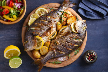 Grilled fish with roasted potatoes, lemon and rosemary on wooden tray. View from above, top