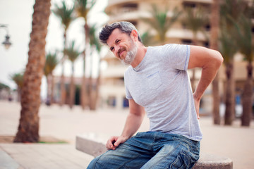 Man with back pain sitting on bench at the outdoor. People, health care and medicine concept