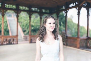 Beautiful curly hair girl in a light blue simple dress in a pavilion in a garden