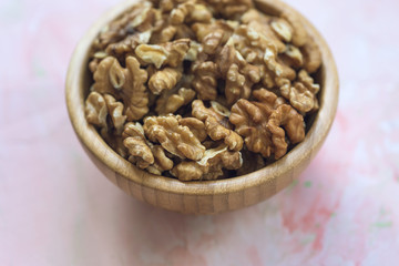 Fototapeta na wymiar Walnuts kernels, peeled nuts in a wooden bowl on a pink background