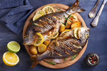 Grilled fish with roasted potatoes, lemon and rosemary on wooden tray. View from above, top