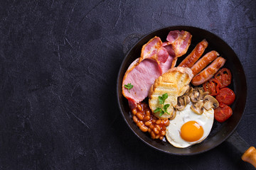 Full English or Irish breakfast with sausages, bacon, eggs, tomatoes, mushrooms and beans on black...