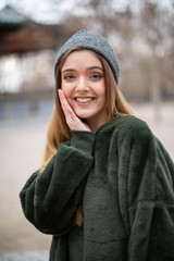 Portrait of happy smiling young blond woman with winter hat in a park in autumn	