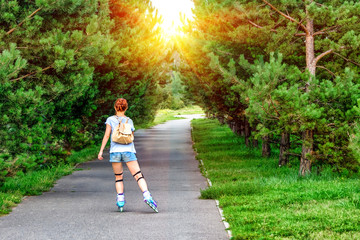 Sporting girl rollerscating in park fir alley on summer day.