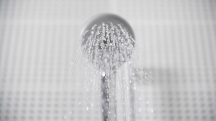 Close-up of turning on and off shower head in bathroom, white tiles with black pattern on the walls, focus on water sprays out and flowing slowly, falling drops
