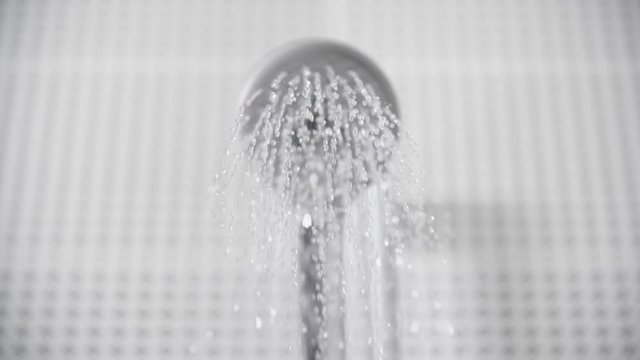 Close-up of turning on and off shower head in bathroom, white tiles with black pattern on the walls, focus on water sprays out and flowing slowly, falling drops