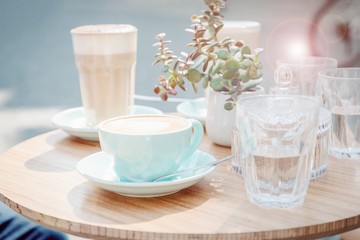 Mint cup of coffee cappuccino and glass with coffee latte in a street cafe. Sun glare effect. Pastel toned photo