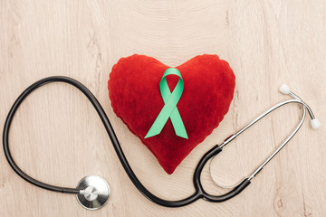 top view of toy heart, stethoscope and green ribbon on wooden background
