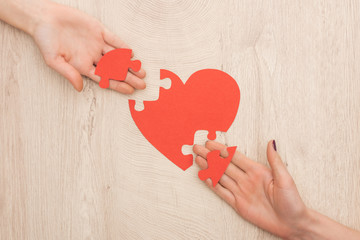 cropped view of women holding pieces of puzzle and paper heart