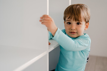 Portrait of a little boy in blue at home standing in the book shelf