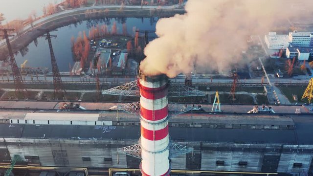Aerial circling view of fuming chimney of CHP plant (coal-fired power station) at sunset