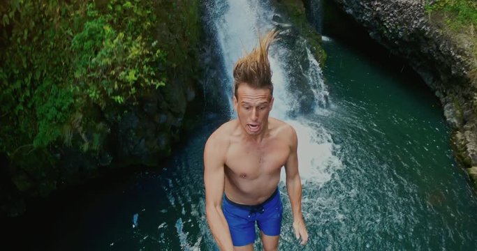 POV shot of young man cliff jumping with waterfall