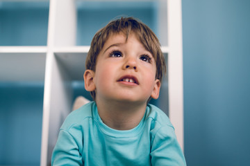 Portrait of a little boy in blue at home lying in the book shelf on the floor hiding games