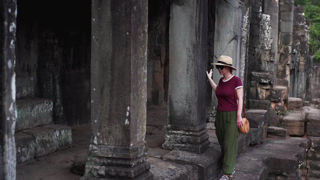 Woman tourist is walking among ruins of Bayon Temple, a Khmer temple at Angkor in Cambodia built in the late 12th or early 13th century and richly decorated