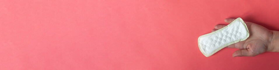 woman's hand holding a sanitary pad on the pink background. A large banner size photo of a hand holding a feminine hygiene pad