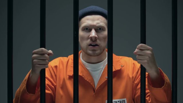 Aggressive dangerous male prisoner with scar on face holding bars and shouting