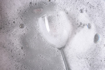 A dishpan with a single wine glass immersed in soapy water