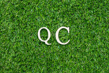 Wood alphabet letter in word QC (Abbreviation of Quality Control) on green grass background