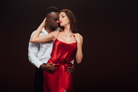 african american man embracing beautiful seductive woman in red dress isolated on black with copy space