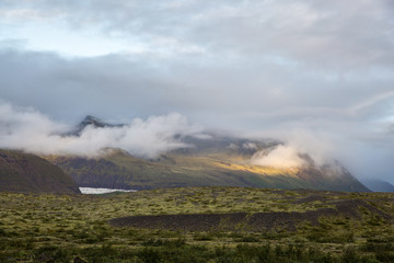 Lava field covered with moss and lichen, in the background you can see mountains in white clouds