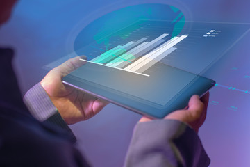 Someone who uses digital tablets with technology in business. Using the bar diagram data, in the form of a hologram. The technology concept of the business world.