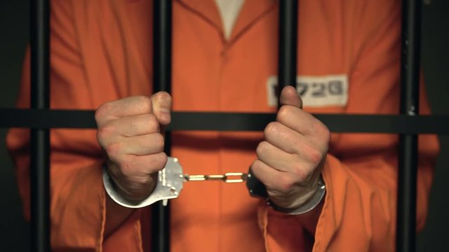 Prisoner showing hands in handcuffs, dangerous criminal standing behind bars
