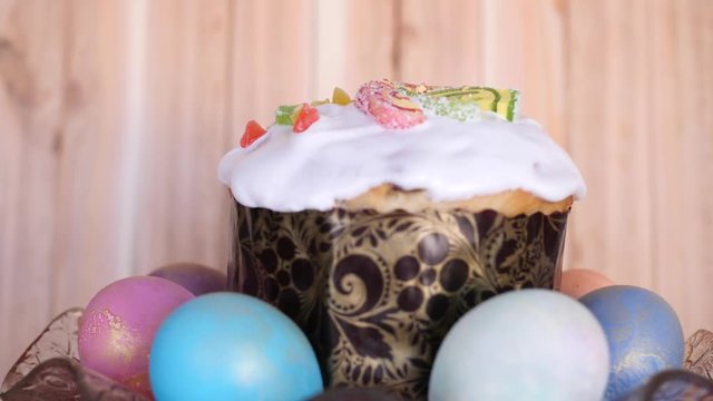 a traditional Easter cake decorated with glaze and candied fruits with colored easter eggs are rotating in beautiful glass plate on wooden background in slow motion middle shot 4K video with no people