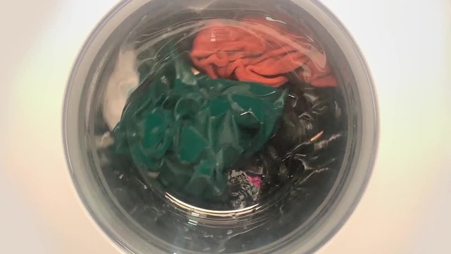Slowmotion shot in center of the working washing machine. Washing machine is cleaning soaked clothes. Laundry cleaning.