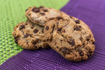 Three cookies with chocolate chips isolated on a purple and green tablecloth