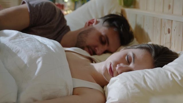 Young cute Caucasian couple sleeping together in bed, woman almost wakes up because of dream. Harmony, health concept. Married couple, loving young people, comfort concept. Close up view