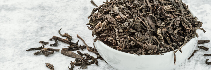 Dried tea is poured into a white ceramic cup on a marble table.