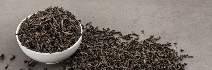 Dried tea is poured into a white ceramic cup on a gray textured background.