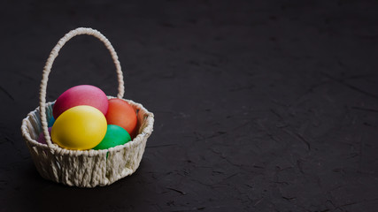 Colored easter eggs in a basket on a black background