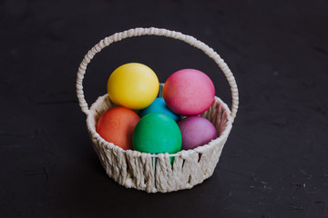 Colored easter eggs in a basket on a black background