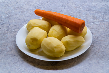Peeled potatoes and carrot on a white plate, kitchen countertop on background, Potato and carrot From the side photo
