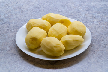 Peeled potatoes on a white plate, kitchen countertop on background, Potato and carrot From the side photo