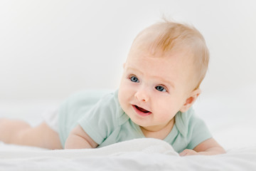 Portrait of beautiful infant baby lying on stomach in bed