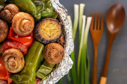 Baked vegetables in foil - tomatoes, eggplants, peppers on a gray wooden table background. View from above. Close-up