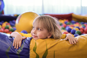Portrait of a blond boy in a yellow t-shirt. The child smiles and plays in the children's playroom. Ball pool.