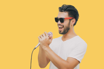 Asian handsome man with a mustache, smiling and singing to the microphone isolated on yellow...