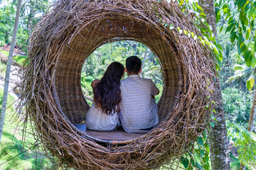 Asian woman and man enjoying his time sitting on a bird nest in the tropical jungle near the rice...
