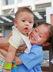 Happy little Asian sister carrying her little brother.