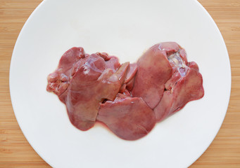 Raw fresh chicken liver in white plate on wooden board background.