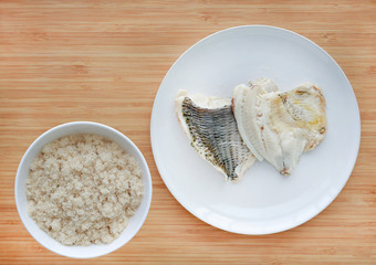 Steamed tilapia fish fillet with dried shredded fish floss in white plate on wooden board background.